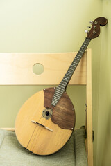 Traditional Russian domra stringed musical instrument resting against a wooden chair with green wall background