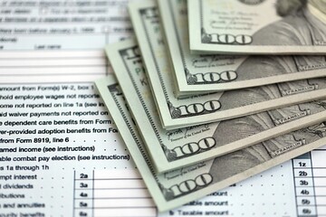 Big amount of United States USD dollar bills on table with 1040 tax return form
