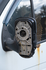 Detailed view of a damaged side mirror housing on an old vehicle, with missing glass and visible inner wires. Symbol of wear, neglect, or vandalism