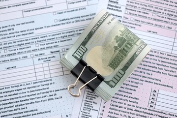 Big amount of United States hundred dollar bills in bunch on table with tax return form