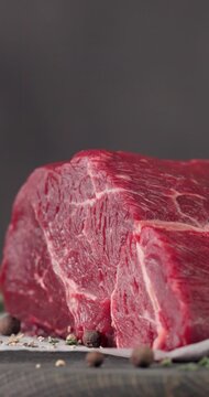 Fresh raw beef meat with pepper and thyme turning on dark wooden cutting board