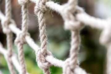 Close-up of a knotted rope net against a blurred green background. The image shows the texture and detail of the rope and knots
