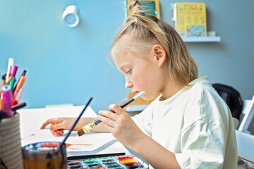 Blond girl child painting with paintbrush indoor. Child 6 years old