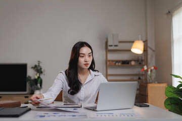 Asian businesswoman working from home office analyzing financial charts on laptop
