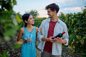 Happy couple enjoying a romantic date at a vineyard, preparing for wine tasting with a bottle and glasses