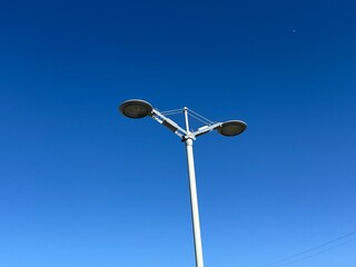 Street light pole with dual lamps against clear blue sky on a sunny day, minimal urban infrastructure and outdoor design.