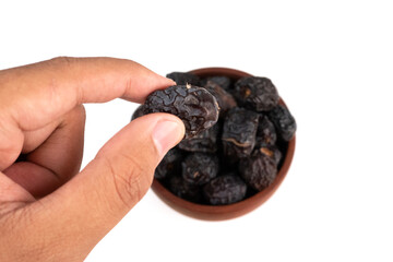 A person's hand is picking up a large, dark date from a small wooden bowl.