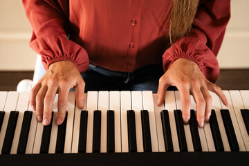Close-up of female hands playing digital piano keyboard with sheet music at home during daytime, concept of online music education and practice indoors © Соня Монштейн