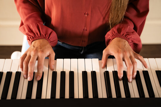 Close-up of female hands playing digital piano keyboard with sheet music at home during daytime, concept of online music education and practice indoors - Powered by Adobe