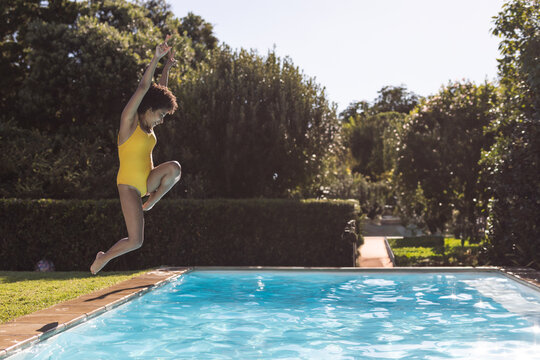African American woman leaping at pool edge in backyard with blue water, copy space
