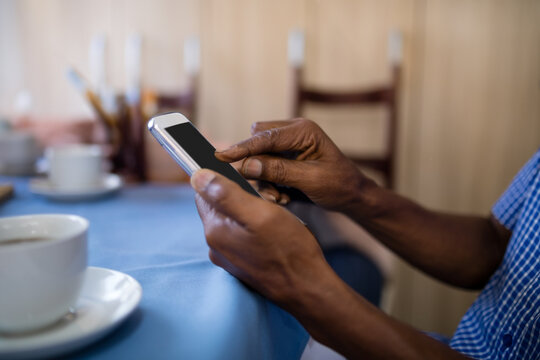 Senior African American man using smartphone at cafe table draped in blue cloth near coffee cup