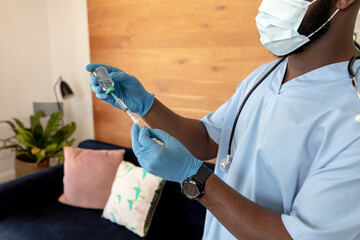 African American male wearing scrubs, stethoscope filling syringe via vaccine vial home, copy space