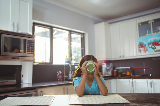 Green mug steaming on wooden table near window with potted plant, microwave on dark countertop