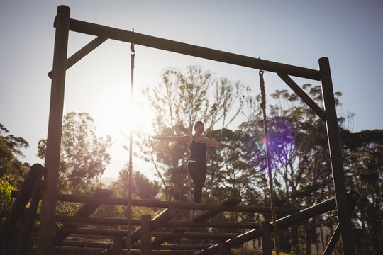 Woman balancing on horizontal wooden beam on forest obstacle course, sun creating lens flare - Powered by Adobe