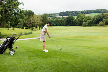 Obraz premium Senior female golfer standing on fairway addressing golf ball with club and push cart, copy space