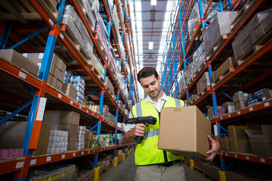 warehouse worker holding box using scanner and capturing barcode in aisle under bright skylight