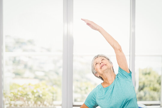 Fototapeta Performing side stretch in turquoise t-shirt in fitness corner by glass wall overlooking garden