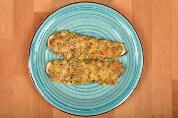 Two halves of baked stuffed zucchini with melted cheese are presented on a light blue plate over a wooden surface