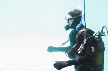 Scuba diver wearing full scuba gear with mask, regulator and BCD drifting in clear blue-green water