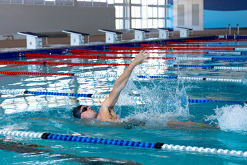 Male swimmer performing backstroke in pool with goggles, black swim cap, red, blue lane dividers