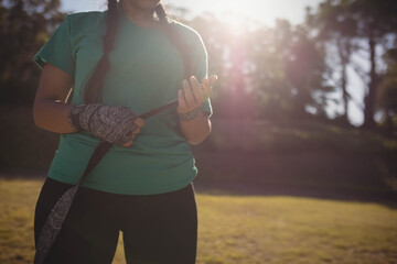 Female athlete adjusting patterned hand wraps in sunlit grassy park area with lens flare