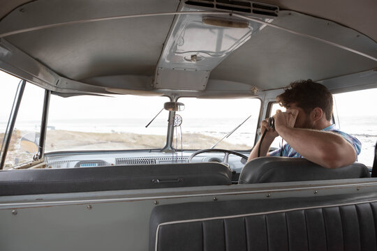 Man holding binoculars peering through windshield of van at beach with mirror ornament copy space