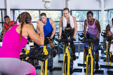 Fitness instructor leading diverse spin class participants pedaling on yellow bikes in gym studio