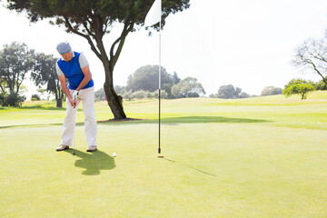 Senior African American golfer lining up putter and ball on putting green by flagstick, copy space