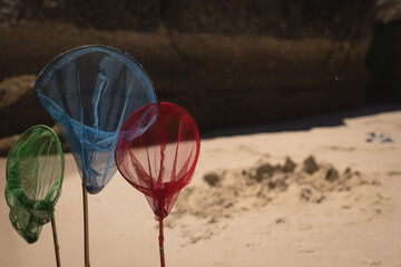Naklejka premium Three multicolored mesh nets are standing in sand on beach near dark rock and sand pile