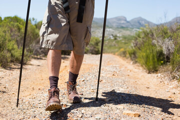 Male hiker walking on dirt trail wearing cargo shorts and boots while gripping black trekking poles