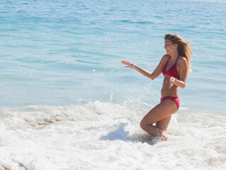 Woman standing knee-deep in breaking ocean waves on sandy beach wearing red bikini, copy space