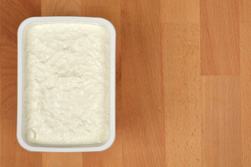 An open package of creamy fresh cheese is placed on a wooden background, ready to be eaten