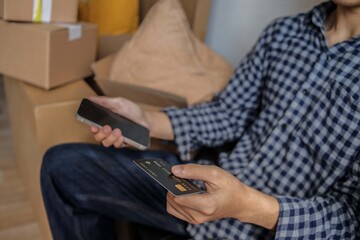 Man Holds Credit Card and Phone Making Payment Amidst Moving Boxes