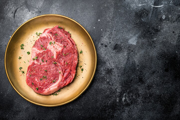 Raw Rib eye steak with herbs and spice in plate, fresh beef meat. black background. top view
