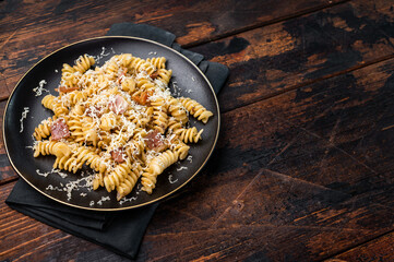 Italian Carbonara pasta topped with crispy bacon bits in a plate. Wooden background. Top view