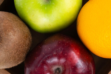 A close up shot of a kiwi, green apple, red apple, and orange inside a wooden bowl.