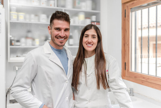Two diverse pharmacists standing in a laboratory pharmacy smiling at camera