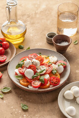 Caprese salad with sliced tomatoes, mozzarella, basil, olive oil on brown textured background