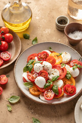 Caprese salad with sliced tomatoes, mozzarella, basil, olive oil on brown textured background