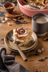 Freshly baked cinnabon bun served on ceramic plate and coffee cup on wooden textured background