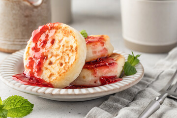 Cottage cheese pancakes or syrniki with raspberry jam on ceramic plate on light gray kitchen table close up. Healthy sweet breakfast