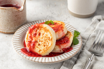 Cottage cheese pancakes or syrniki with raspberry jam on ceramic plate on light gray kitchen table. Healthy sweet breakfast