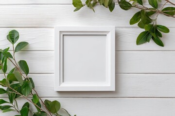 Blank white frame surrounded by fresh green leaves on a white wooden surface