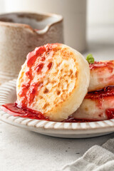 Cottage cheese pancakes or syrniki with raspberry jam on ceramic plate on light gray kitchen table close up. Healthy sweet breakfast