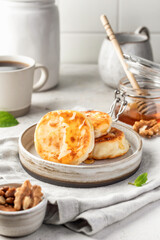 Cottage cheese pancakes or syrniki with walnuts and honey on ceramic plate on light gray kitchen table. Healthy sweet breakfast