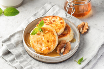 Cottage cheese pancakes or syrniki with walnuts and honey on ceramic plate on light gray kitchen table. Healthy sweet breakfast