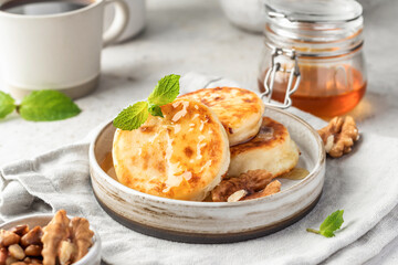 Cottage cheese pancakes or syrniki with walnuts and honey on ceramic plate on light gray kitchen table. Healthy sweet breakfast