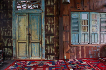 Weathered wooden door and window adorn rustic building with colorful carpet, evoking a sense of...