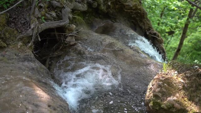  A waterfall on a mountain stream, the edge of a waterfall from where the water begins to fall. The camera makes a crane movement upwards revealing a wider scene. Blederija waterfall in Eastern Serbia