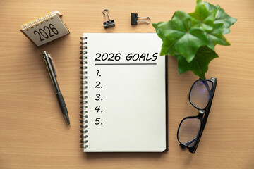 Notebook titled 2026 Goals with blank checklist on a wooden desk with pen glasses mini calendar and laptop, ideal for life and business goal planning strategy and personal growth in the new year.